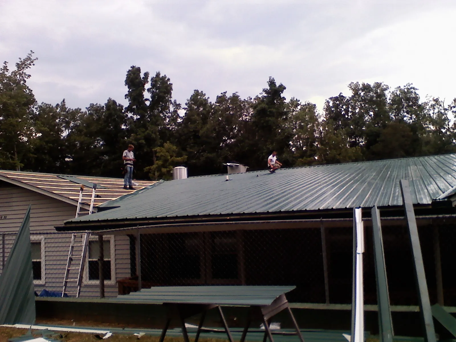 Two roofers installing green metal panels above a covered porch in Rockmart