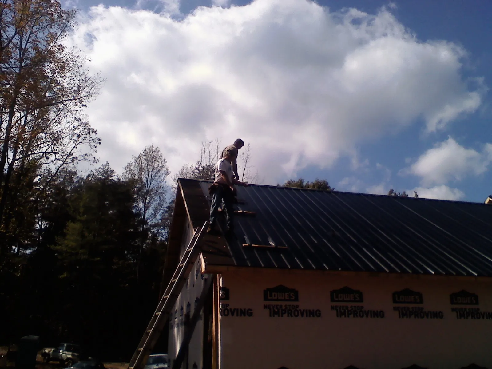 Roofer fastening dark metal panels high against a cloudy sky, from a Roof Inspection job in Rockmart