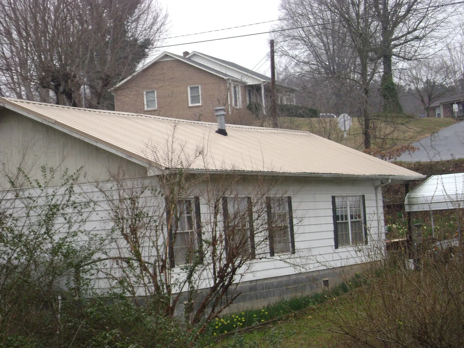 Tan metal roof on a white sided house set into a hillside — Commercial Roofing by Roofing Brothers in Rockmart